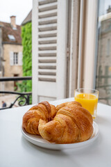 French breakfast, fresh baked croissant buttery pastry served with orange juice and old french houses on background