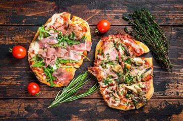 Sliced pizza with prosciutto parma ham, arugula and parmesan cheese. Dark wooden background. Top view