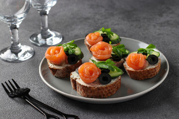 Sandwiches with salmon, cucumber, cream cheese and black olives on gray background. Homemade holiday snack.