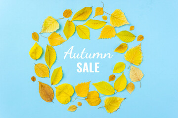 The word SALE on light blue background surrounded by autumn yellow leaves. Fall shopping concept. Flat lay, top view