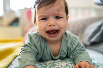 Front view on unhappy small caucasian baby lying on the bed crying by her mother due cramps or...