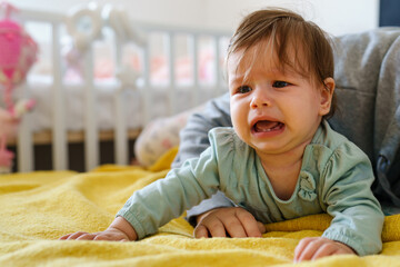 Front view on unhappy small caucasian baby lying on the bed crying by her mother due cramps or...