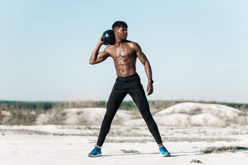 Fitness African American man doing workout twist exercise with medicine ball weight, outdoors on nature