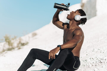 African muscular man, drinks water in a reusable bottle, man with water after training on a sunny...