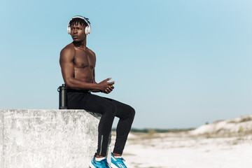 muscular happy african american man, listening to music with headphones relaxing after jogging in nature in mountains