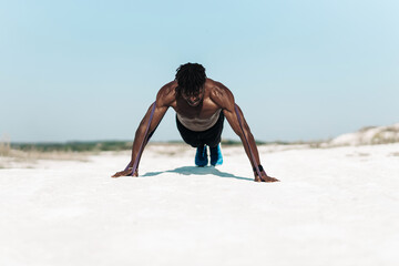 Athletic African man doing push-ups with elastic band as additional difficulty, outdoors