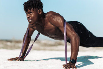Athletic African man doing push-ups with elastic band as additional difficulty, outdoors