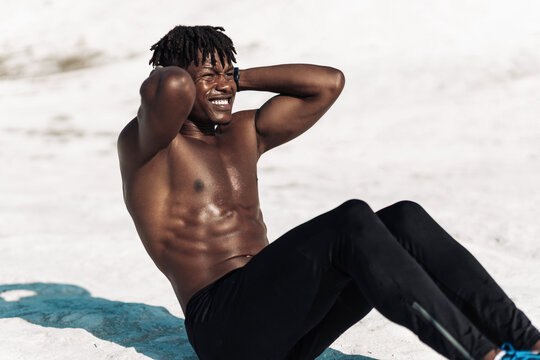 muscular black man, with bare chest, doing abdominal exercises, fitness man working on abs lying on the floor outdoors