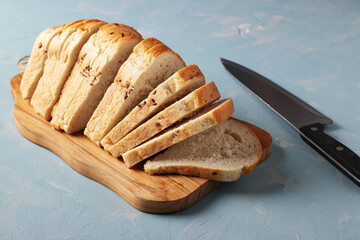 Sliced curly bread made from wheat flour with sesame seeds on a wooden board on light blue background. Closeup