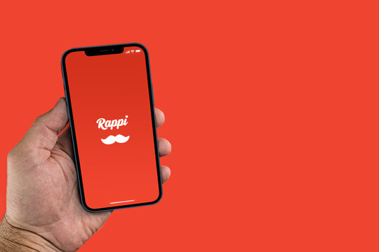 Male hand holding a smartphone with Rappi App on the screen. Red background. Rio de Janeiro, RJ, Brazil. October 2021.