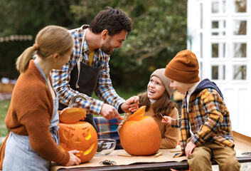 Fototapeta premium Father and children carving pumpkin for halloween in backyard