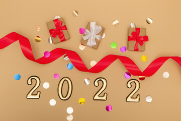 New Year 2022. Top view New Year mockup on beige background: red ribbon, gift box, gold numbers and multicolored sparkles. Layout of postcards, invitations.