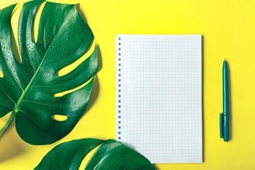 Fototapeta na wymiar Monstera leaves, checkered notebook and pen on trendy yellow background. Copy space