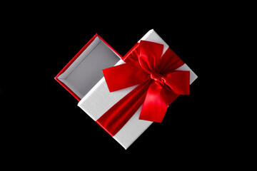 Open white gift box with red satin bow on black background. Flat lay, top view, copy space