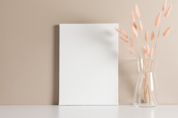 White canvas mockup with dry lagurus on beige wall background. Front view