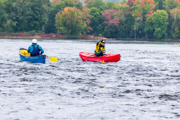 Fototapeta na wymiar Two canoeists practice paddle strokes on a rainy fall day during a “moving water” paddling course. At Palmer Rapids on the Madawaska River an iconic paddling destination in Eastern Ontario, Canada