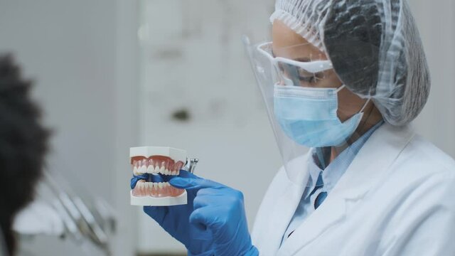 Orthodontics treatment. Professional woman dentist showing plastic jaw cast to male patient and explaining cure plan
