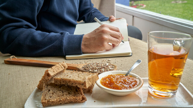 Latin European male student busy learning lessons during lunch at cafe, sitting at table with food and textbooks, making notes, writing down new words preparing for Spanish clas