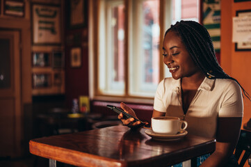 African american woman using a smartphone while drinking coffee in a cafe