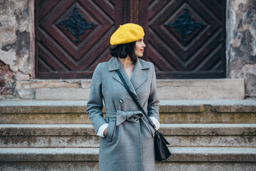 Woman using smartphone and wearing yellow beret and a gray coat