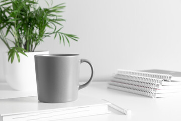 Gray mug mockup with notebook and green plant in pot on white table. front view