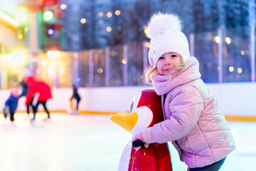 A little girl is skating on an ice rink, holding on to a support, a child is learning to skate,...