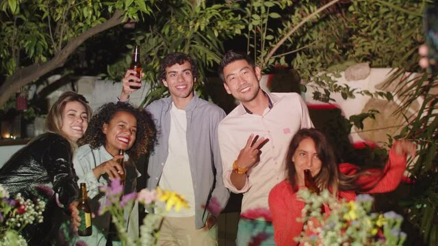 Slider shot of happy people taking picture together at party. Long shot of smiling friends having fun in backyard, posing for camera, laughing, spending time together on weekend. Night party concept