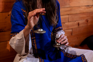 Woman holds a pair of bells in her hands. She has a medieval blue dress and orange background