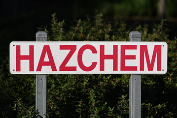 A white hazchem sign with bright red lettering, held up by two steel posts.  The dirty sign sits in...