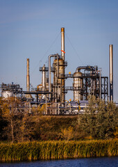 Obraz premium Image of an industrial complex located next to a marsh. There is a maze of shiny metal piping and equipment taken on a sunny day.