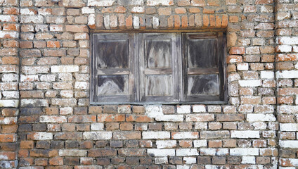 the old brown wooden window is closed on the brown brick wall. the ancient portrait of the abandoned old building.