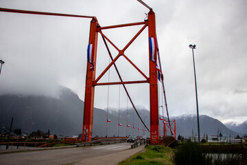 Fototapeta na wymiar Suspension bridge in Aysén, Southern Chile. Patagonia. Painted in red in front of the mountain.
