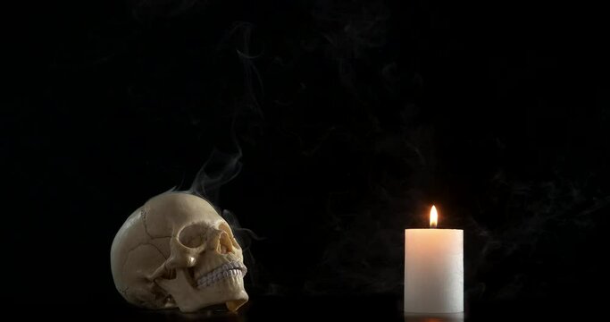 Attributes for magic. A view of smoking skull and a burning candle in the dark room. A concept of magic attributes in the black background.