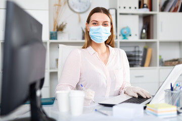 Fototapeta na wymiar Businesswoman in protective mask working alone with laptop and papers in office, new normal due to coronavirus outbreak