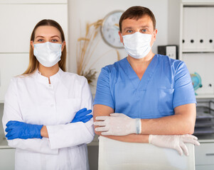 Fototapeta na wymiar Portrait of two professional qualified health workers wearing disposable surgical masks and latex gloves in modern medical office