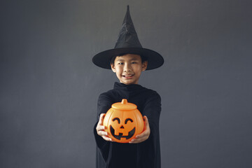 Cute Asian boy celebrating Halloween by wearing witch costume and holding Halloween decoration...