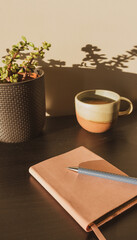 Vertical closeup of pen and journal on table in sunlight with cup and plant in background - selective focus and vintage filter effect