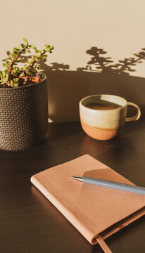 Vertical closeup of pen and journal on table in sunlight with cup and plant in background - selective focus and vintage filter effect