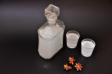 Anise brandy, homemade strong alcohol with a glass bottle and two glasses on a black background.
