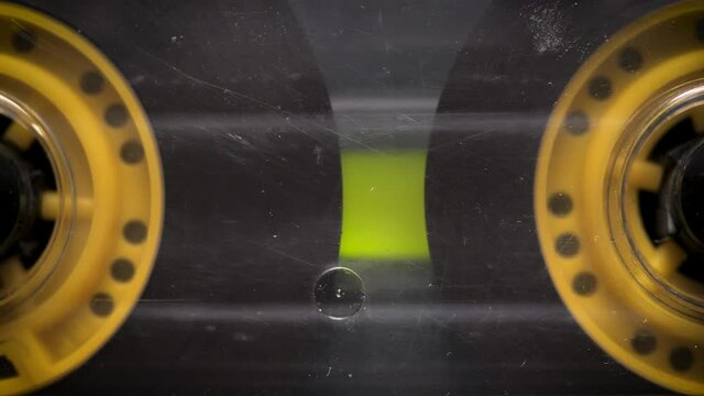 Yellow transparent audio cassette in the tape recorder. Playing and rotating. Close up, macro, front view. Scene A.