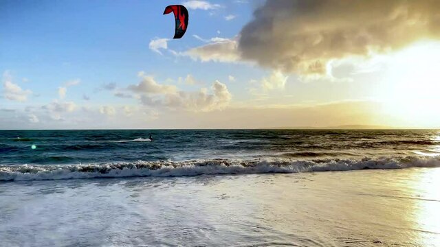 A person kitesurfs on wind and waves in sunset