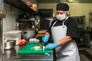 Professional cook cutting onions on a plastic board at kitchen of restaurant