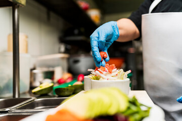 Unrecognizable cook preparing a salad by putting pieces of tomato on top of the other vegetables on a bowl