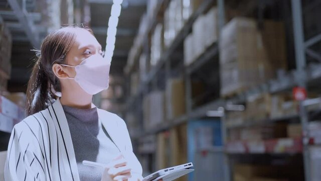 asian woman business owner wear mask use tablet checking amount of stock product inventory on shelf at distribution warehouse factory.logistic business shipping and delivery distribution service