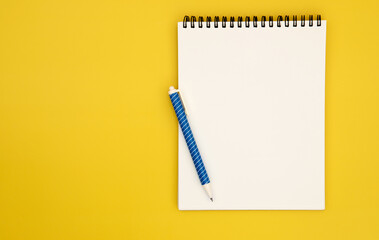 spiral notepad book paper with a blue pen placed on yellow background for creative thinking concept