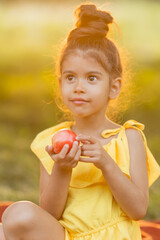 Funny swarthy little girl is eating an apple in the garden. Kid eat fruit outdoors. GMO free food....