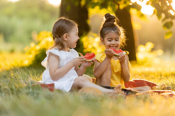 Two kids eating of watermelon in the garden. Kids eat fruit outdoors. Healthy snack for children. Girls enjoying watermelon. The concept of a healthy lifestyle. Happy childhood. Space for text.