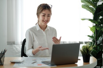Smiling young female employee at home speak talk on video call on laptop with diverse colleagues. Asian woman worker have webcam conference or digital web team meeting or briefing with coworkers