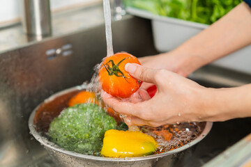 Close up asian young woman washing tomato, broccoli, carrot fresh vegetables, paprika with splash water in basin of water on sink in kitchen, preparing fresh salad, cooking meal. Healthy food people.