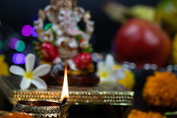 Selective Focus On Golden Brass Diya Deep Illuminated During Diwali Puja New Year Deepawali Ganesh Chaturthi Or Shubh Deepavali Pooja. Ganesha Ganpati Bappa Morya, Flowers, Fruits In Blur Background